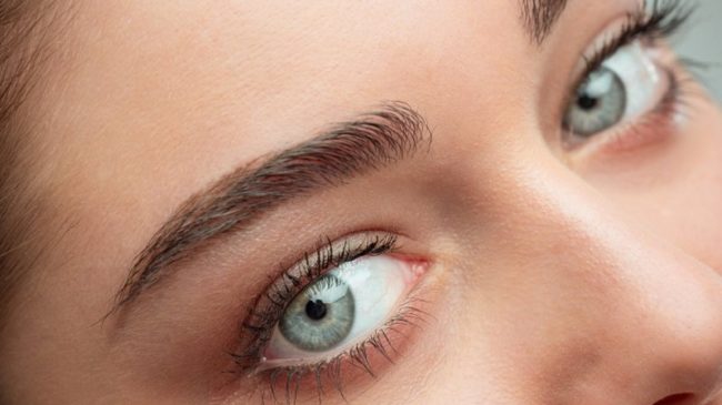 Naheaufnahme eines Gesichts mit betonten Augenbrauen und strahlend blauen Augen.