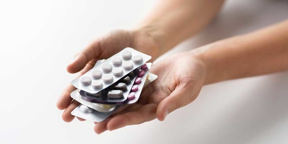 Hände halten mehrere Blisterverpackungen mit unterschiedlichen Tabletten in verschiedenen Farben.