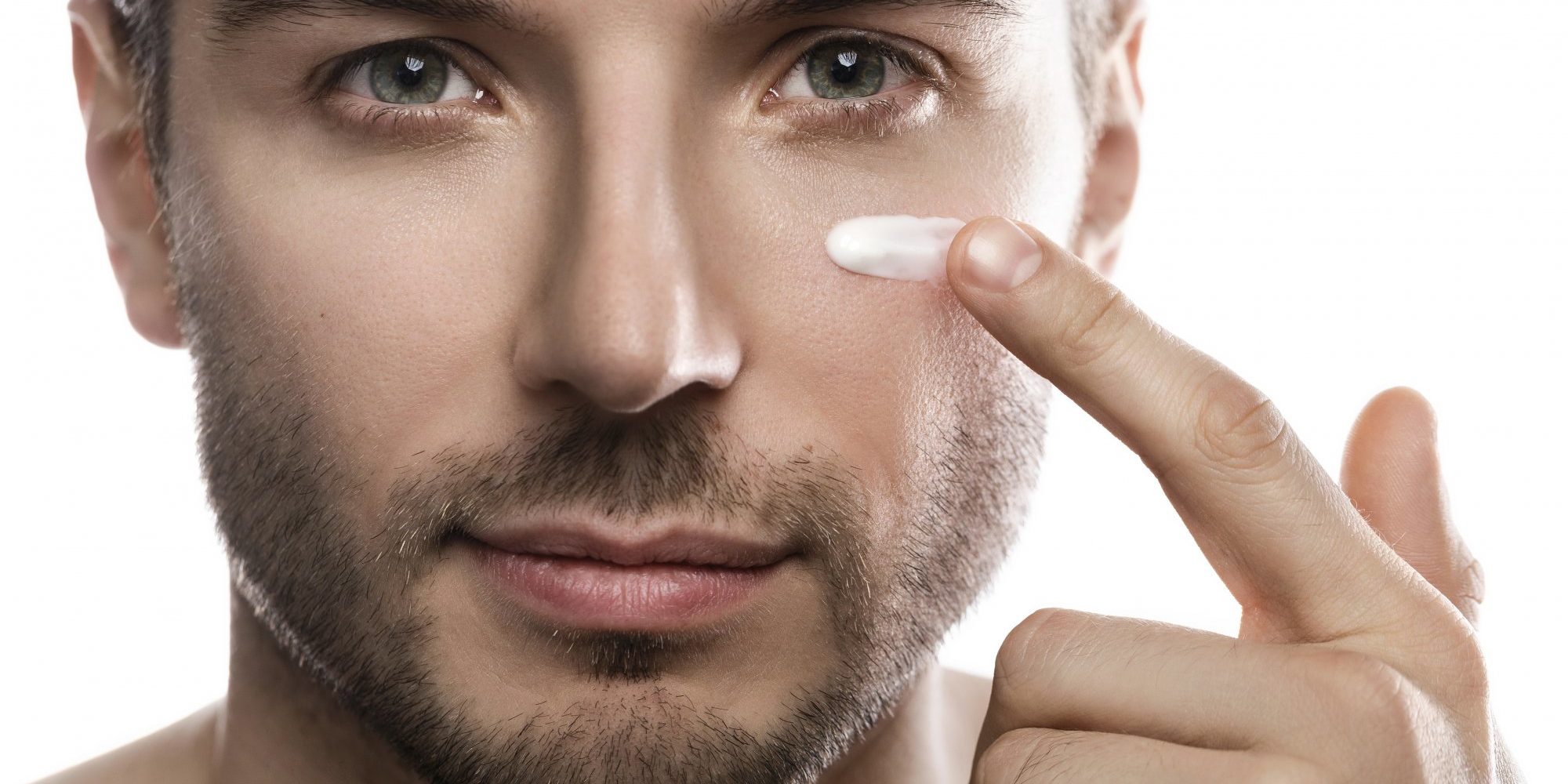 Verletzliche_Maennerhaut.jpg Ein Mann trägt eine Creme auf seine Wange auf, während er in die Kamera schaut. Hintergrund ist neutral.