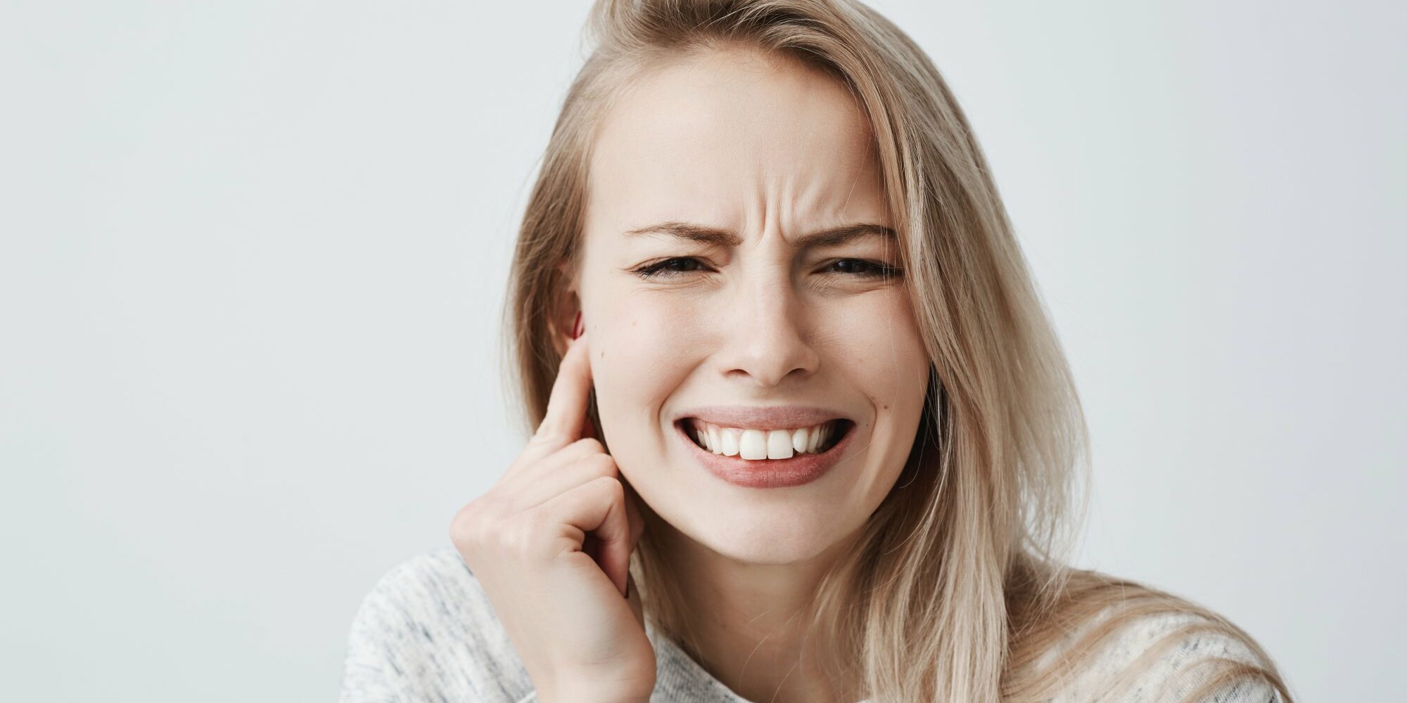 Junge Frau mit schmerzverzerrtem Gesicht, hält sich den rechten Ohrbereich mit der Hand.