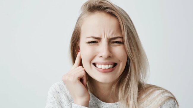 Junge Frau mit schmerzverzerrtem Gesicht, hält sich den rechten Ohrbereich mit der Hand.