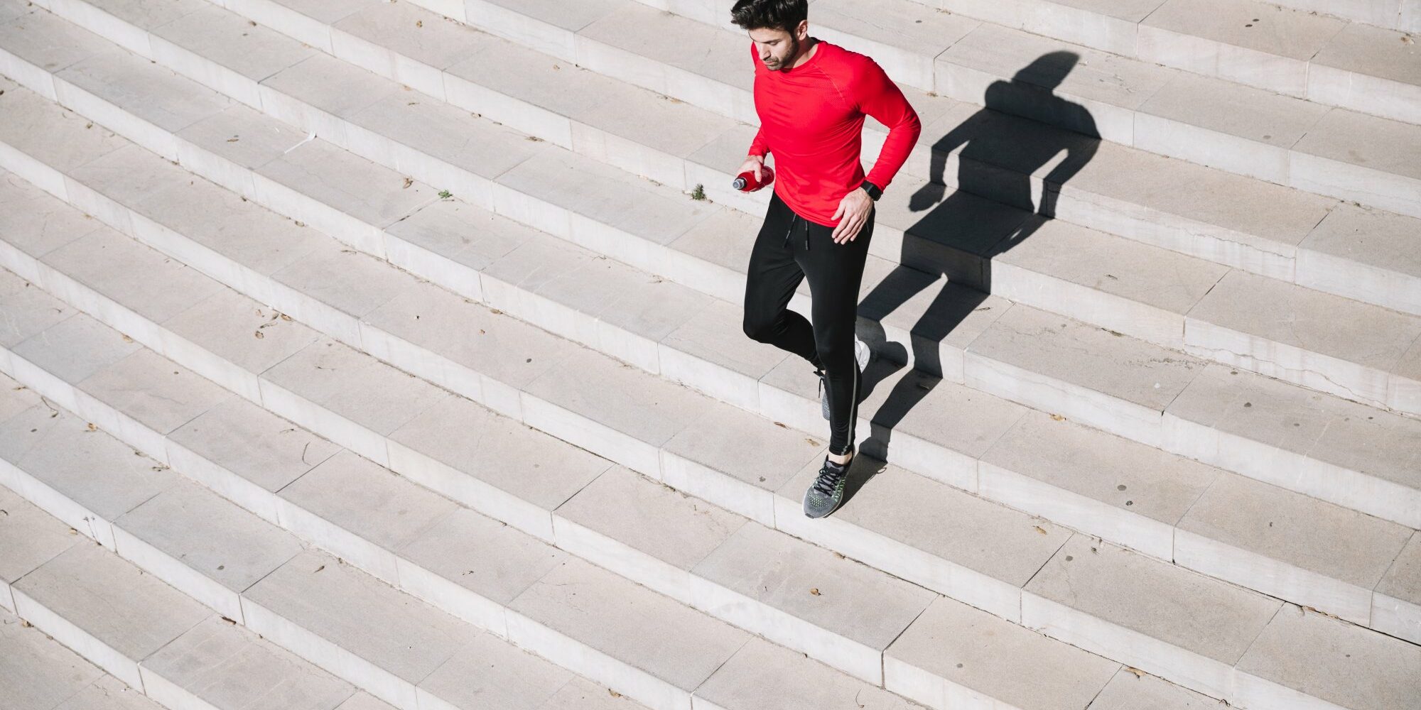 Stiegensteigen_Fitness.jpg Mann in rotem Shirt joggt über eine helle Treppe, sein Schatten ist deutlich sichtbar.