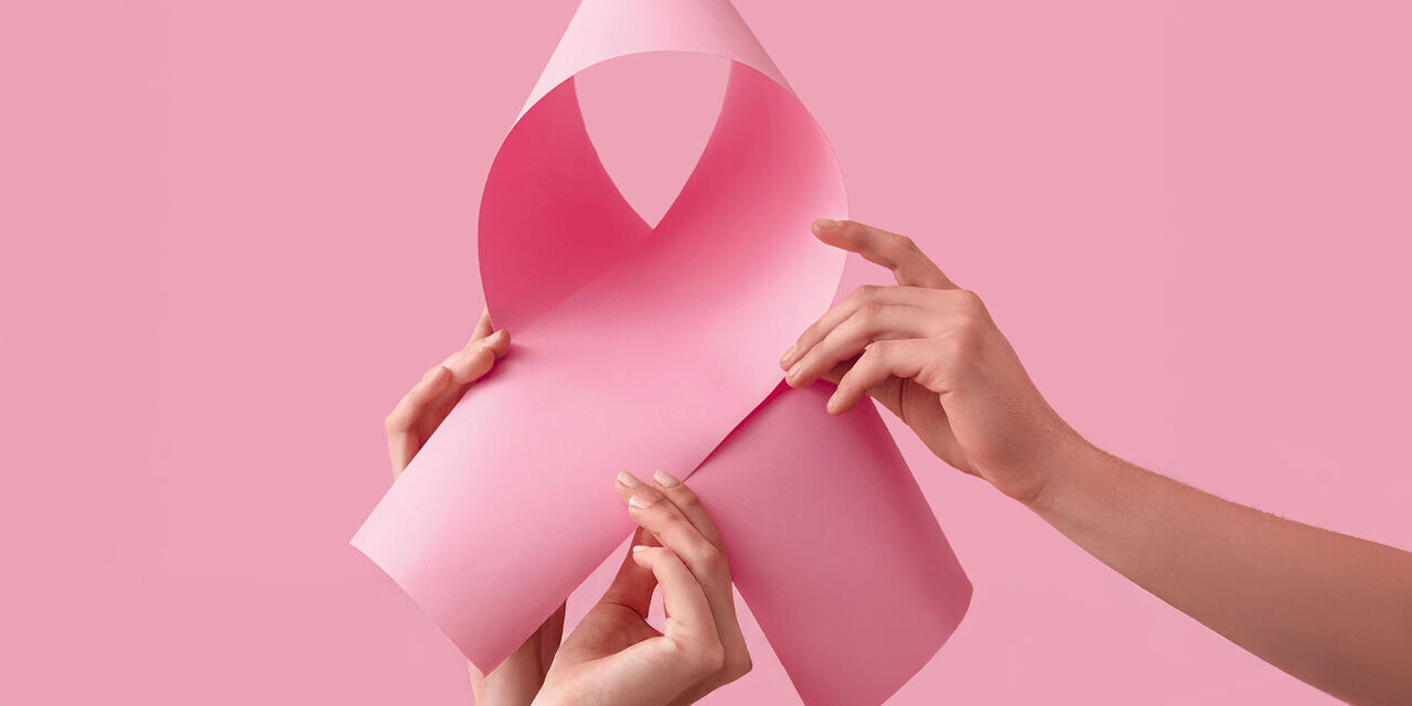 Zwei Hände halten ein rosa Papier, das zu einer Schleife geformt ist, vor einem pinken Hintergrund.