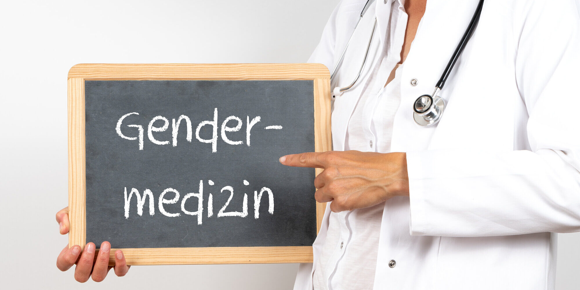 Eine Person in Arztkleidung hält eine Tafel mit der Aufschrift "Gendermedizin".